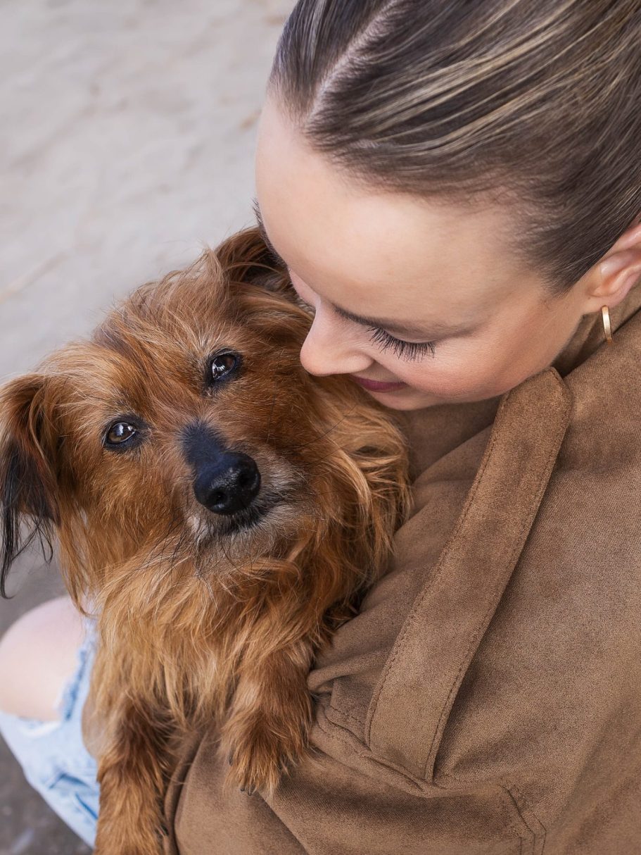 Eine Frau umarmt einen kleinen, braunen Hund mit einem freundlichen Blick.