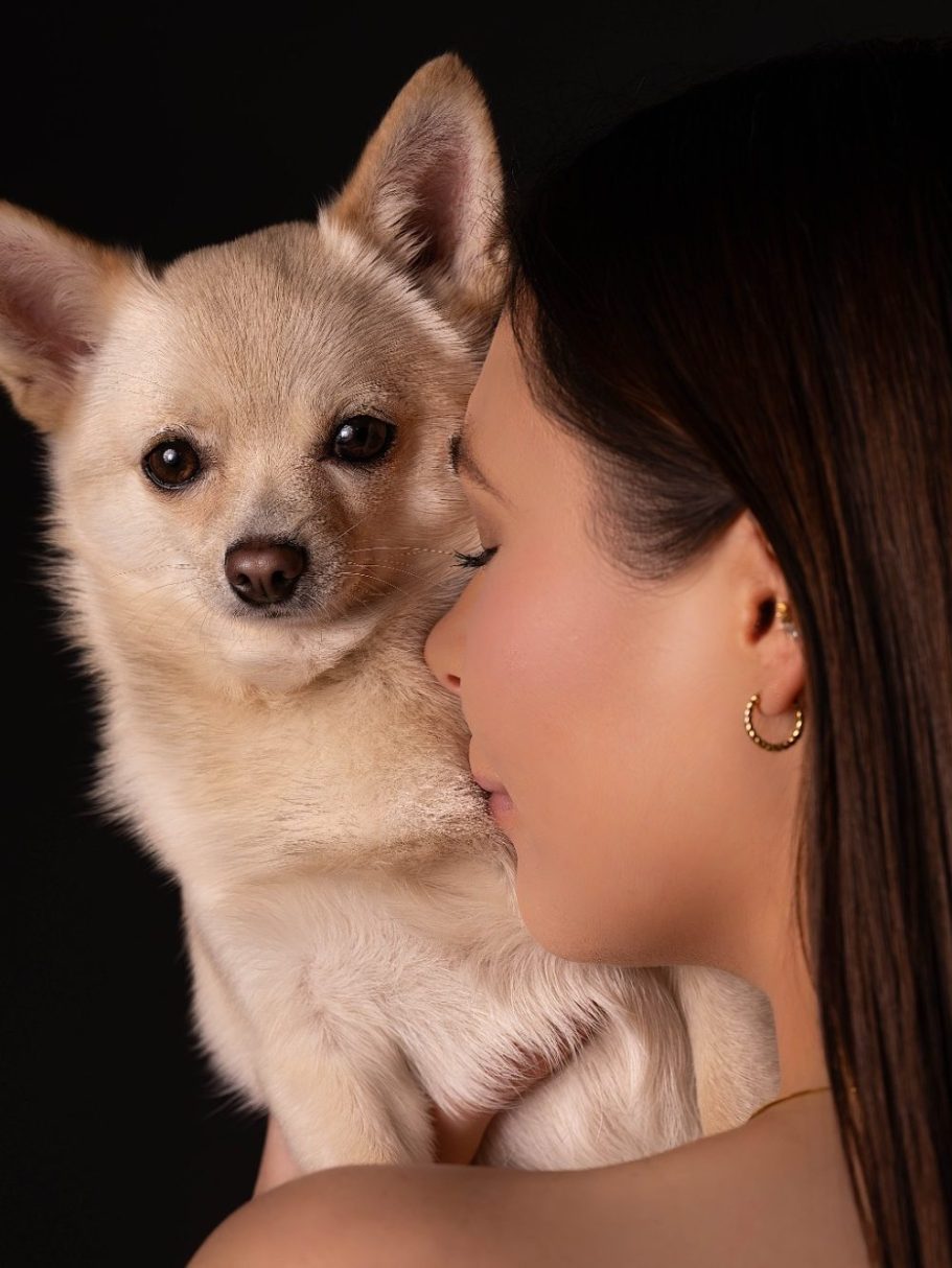 Eine Frau umarmt einen kleinen, hellen Hund, während sie ihm zuneigt.